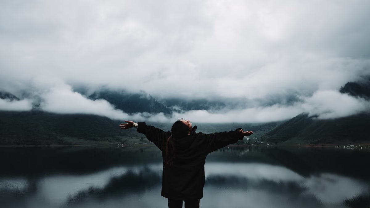 A person enjoys a sense of freedom by a misty mountain lake, embracing nature's tranquility.